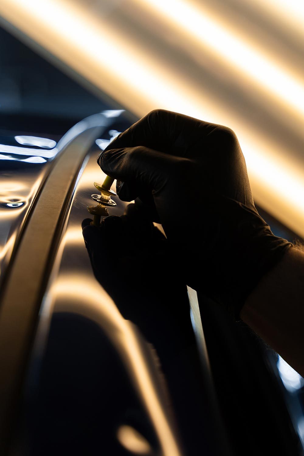 A gloved technician setting a glue tab on a dented body line under PDR lighting