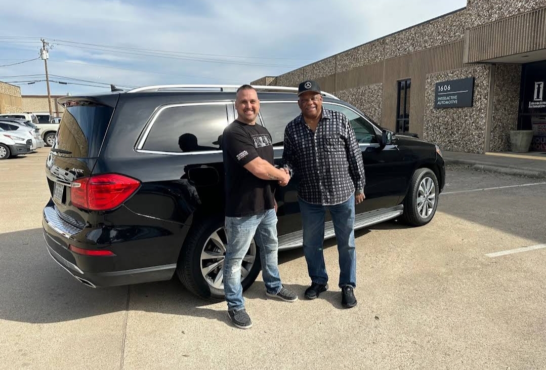 An Auto Hail Damage Solutions owner shaking hands with a customer beside their repaired black Mercedes SUV