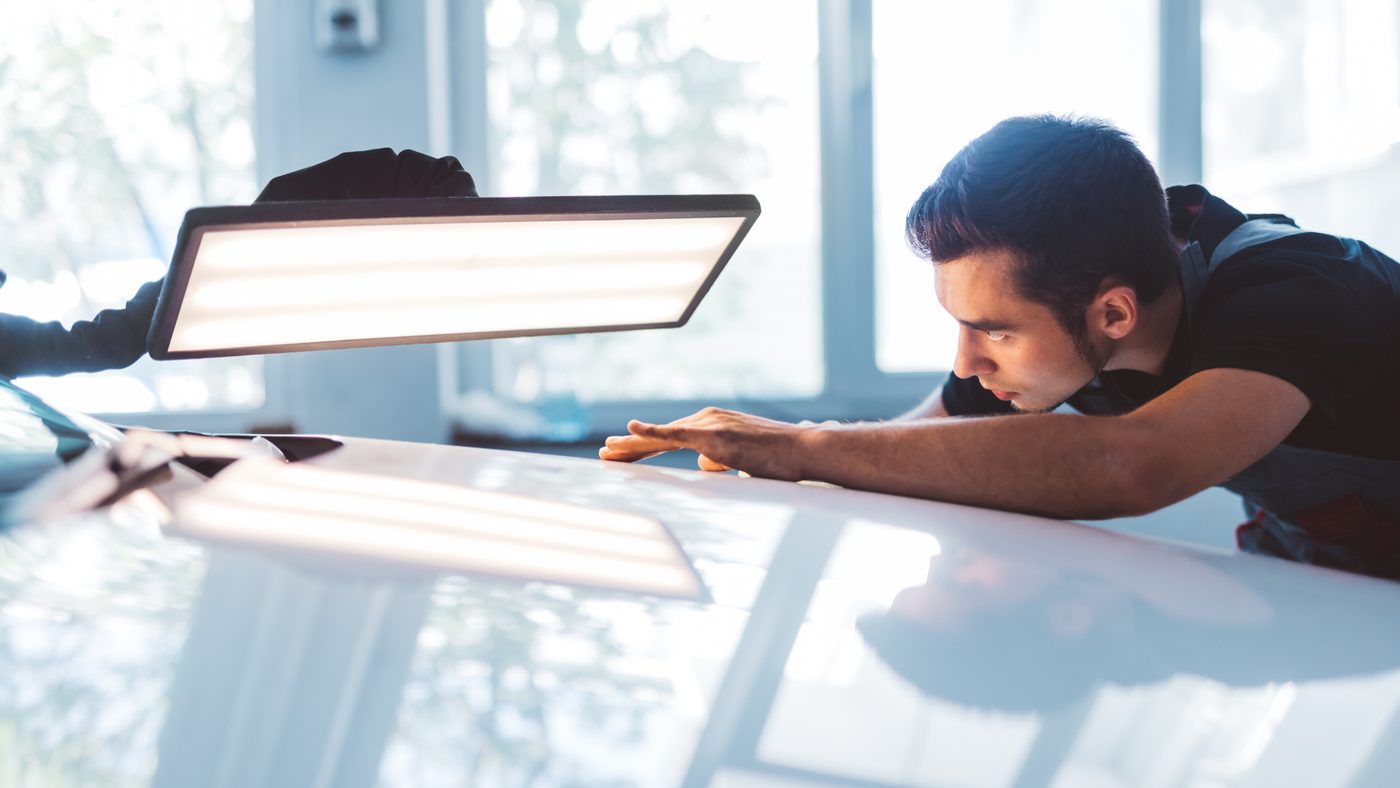 Technician sighting down a panel under a PDR light board to locate dents